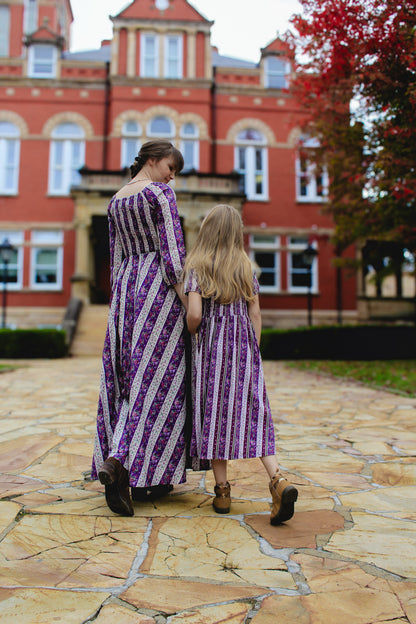 Modest nursing mother and daughter in matching striped dresses outside brick building