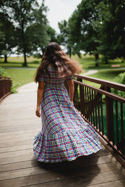 Woman in a plaid modest nursing dress walking on a wooden deck with trees in the background