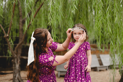 Woman in modest nursing dress adjusting tiara on young girl outdoors