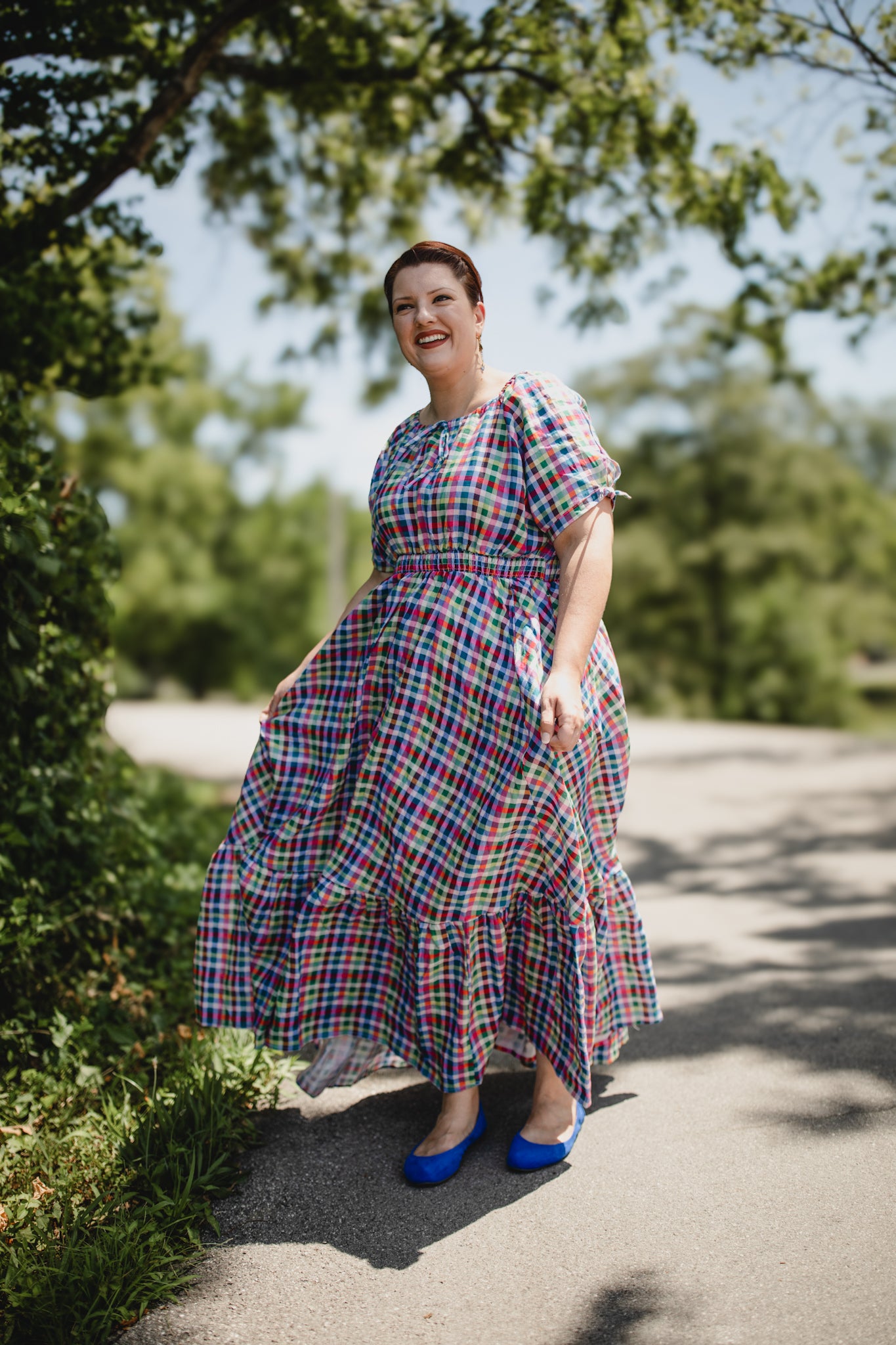 Woman in a plaid modest nursing dress standing on a path with trees in the background