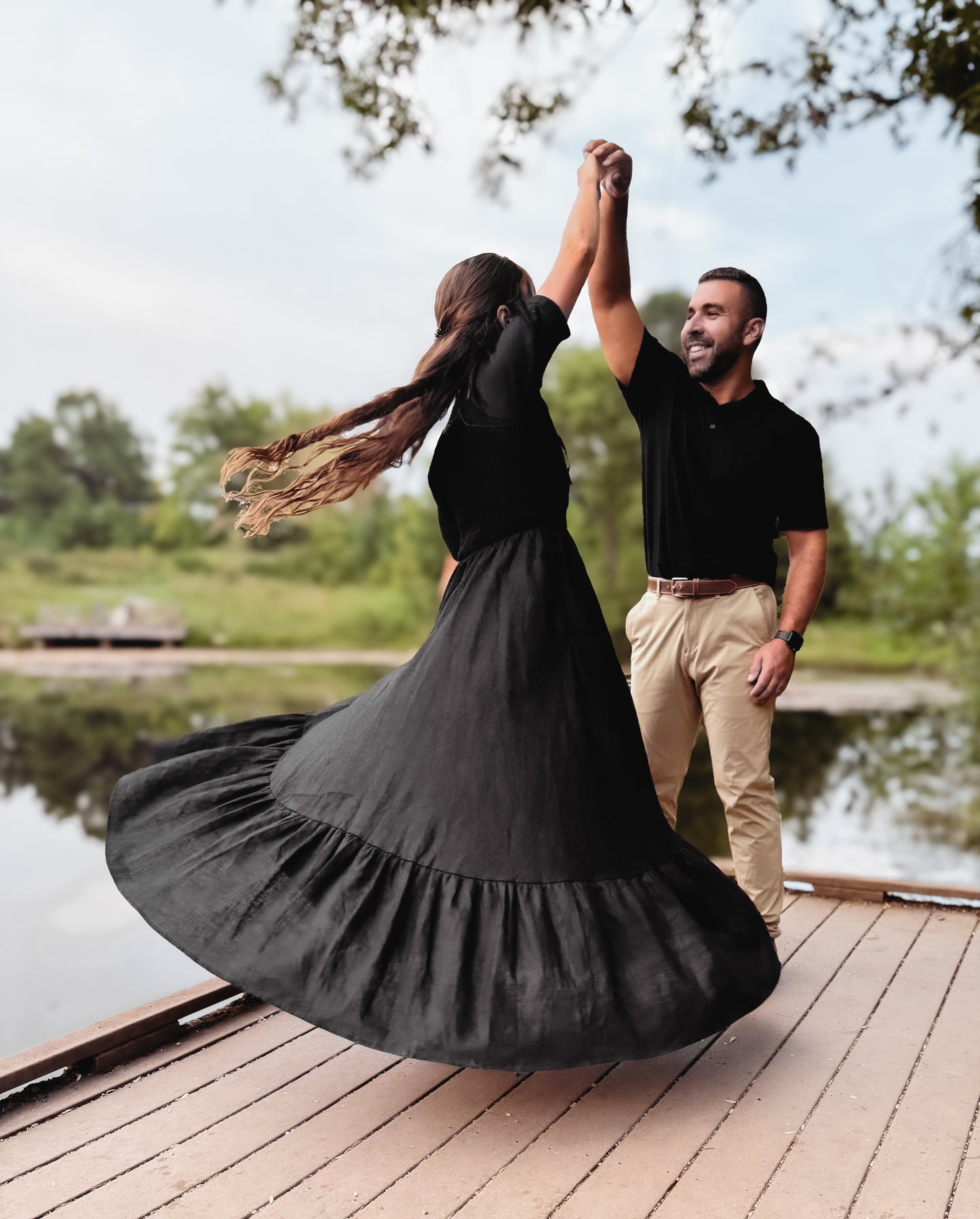 Couple dancing on a wooden dock by a lake with modest nursing dress in the background