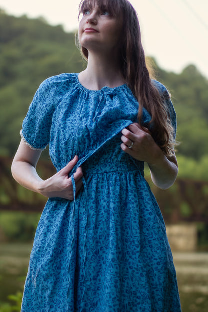 Woman wearing a blue modest nursing dress with a blurred natural background