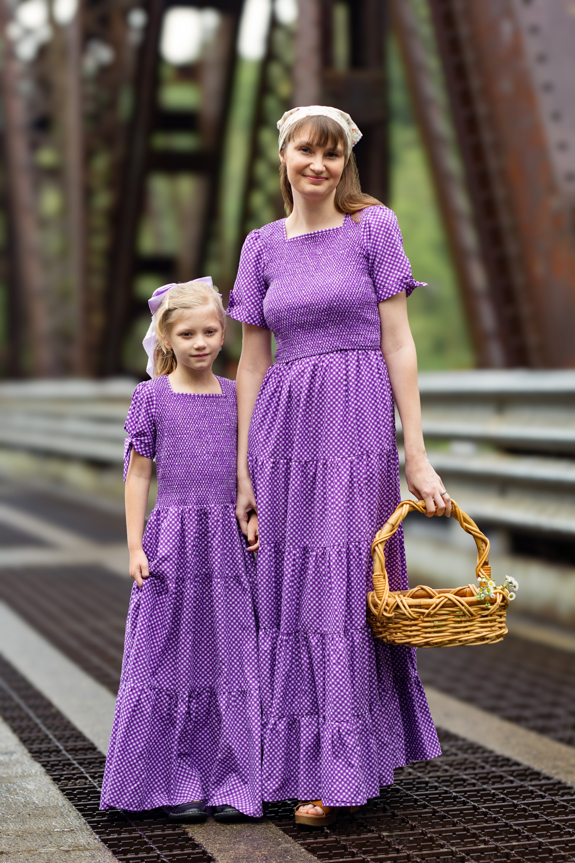 A woman wearing a purple, gingham, five-tiered maxi modest nursing dress with her daughter wearing a matching dress