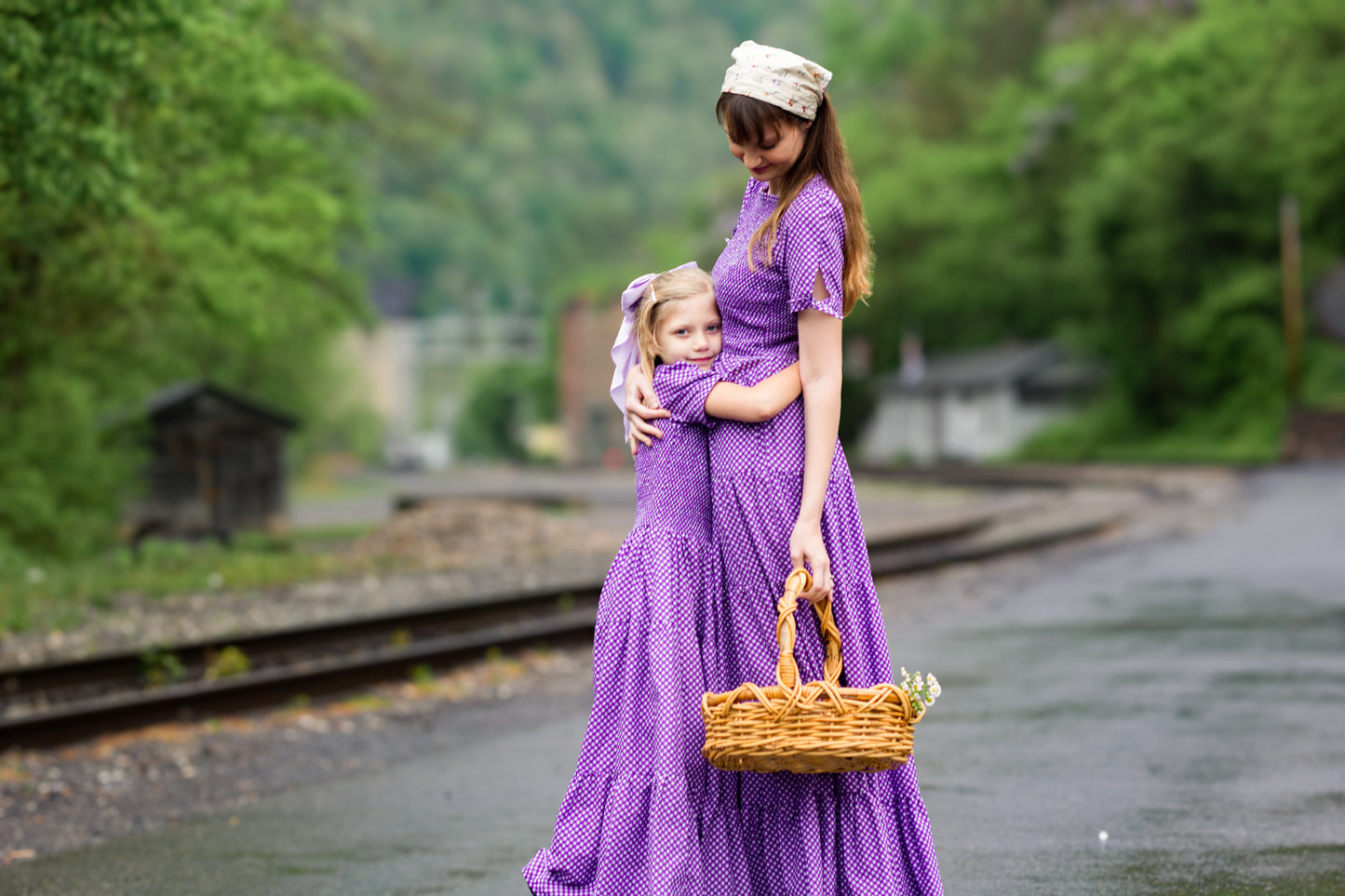 A woman wearing a purple, gingham, five-tiered maxi modest nursing dress with her daughter wearing a matching dress