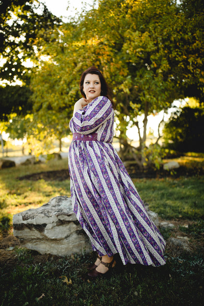 Woman in a modest nursing purple and white striped dress standing outdoors with trees in the background