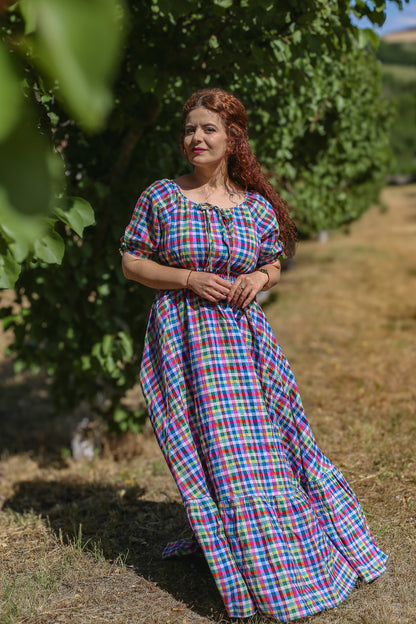 Woman in a colorful checkered modest nursing dress standing in a field with trees in the background