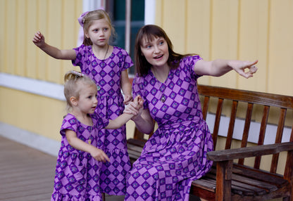 Woman in a purple checkered modest nursing dress with her daughters in matching dresses.
