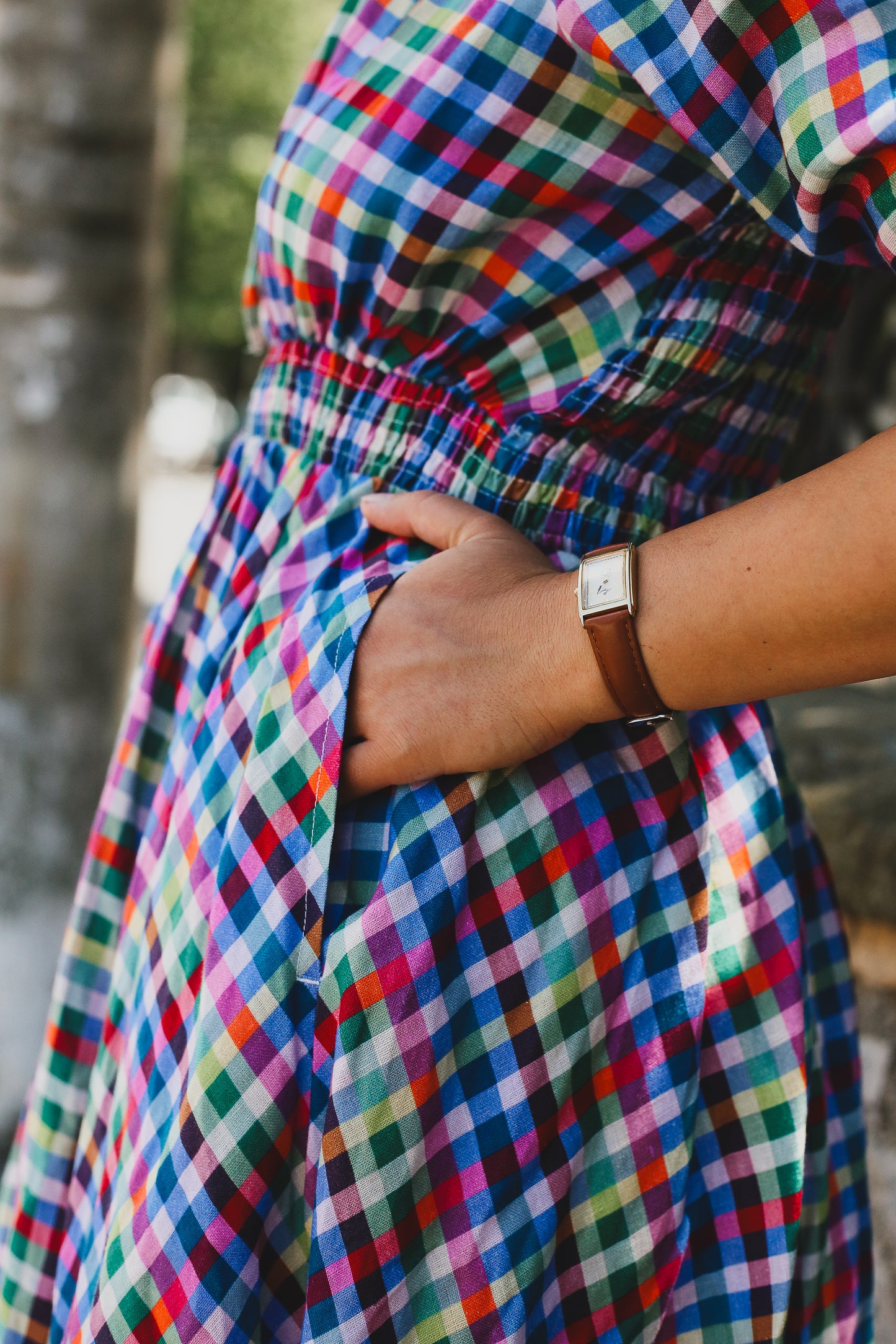 Multicolored checkered modest nursing dress with a wrist wearing a watch, blurred background