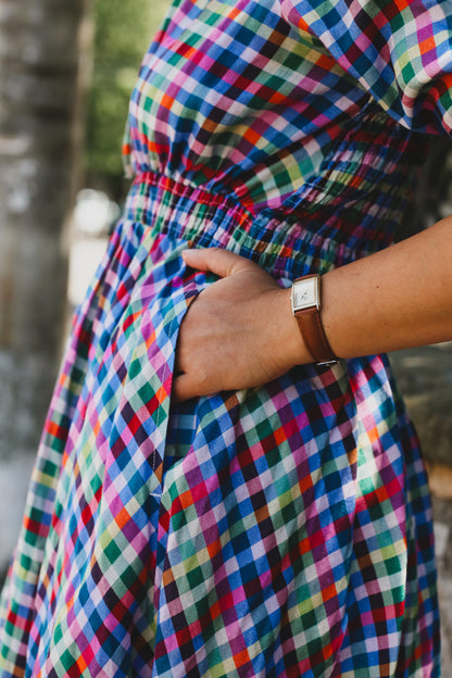 Multicolored checkered modest nursing dress with a wrist wearing a watch, blurred background