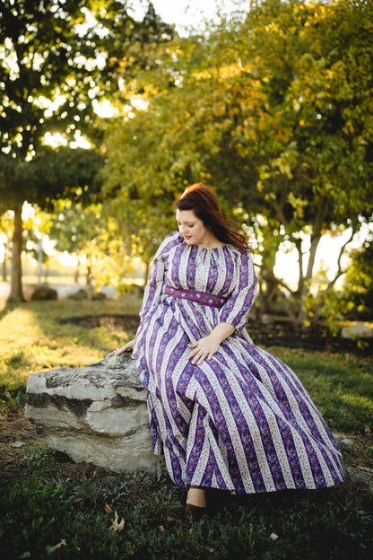Modest nursing woman in striped dress sitting on park rock