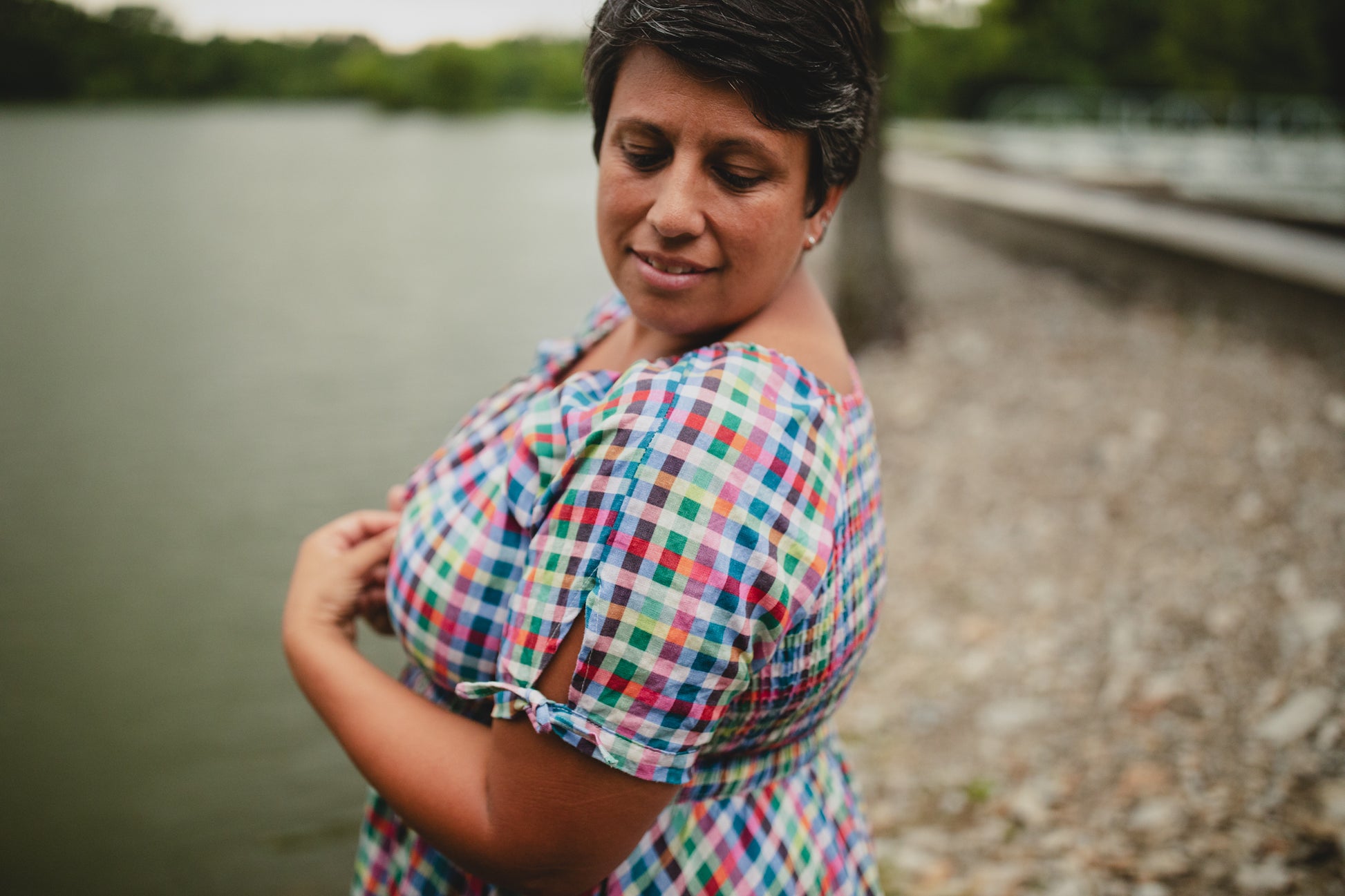 Woman in a colorful checkered modest nursing dress standing by a body of water.