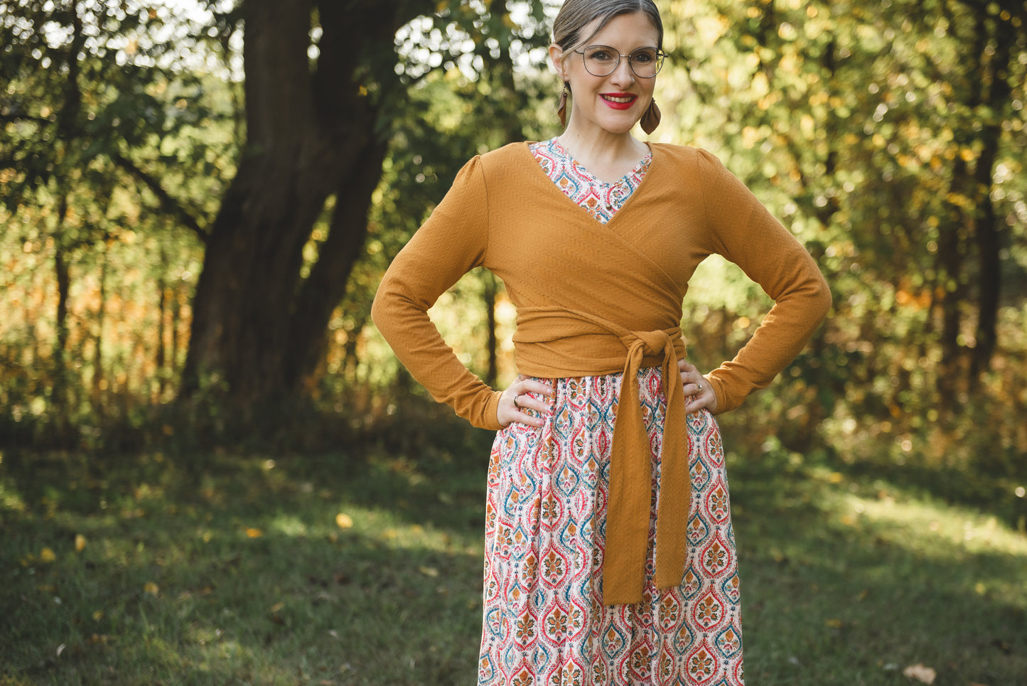 Woman wearing a mustard yellow top and patterned skirt standing in a forest.