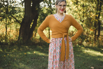 Woman wearing a mustard yellow top and patterned skirt standing in a forest.