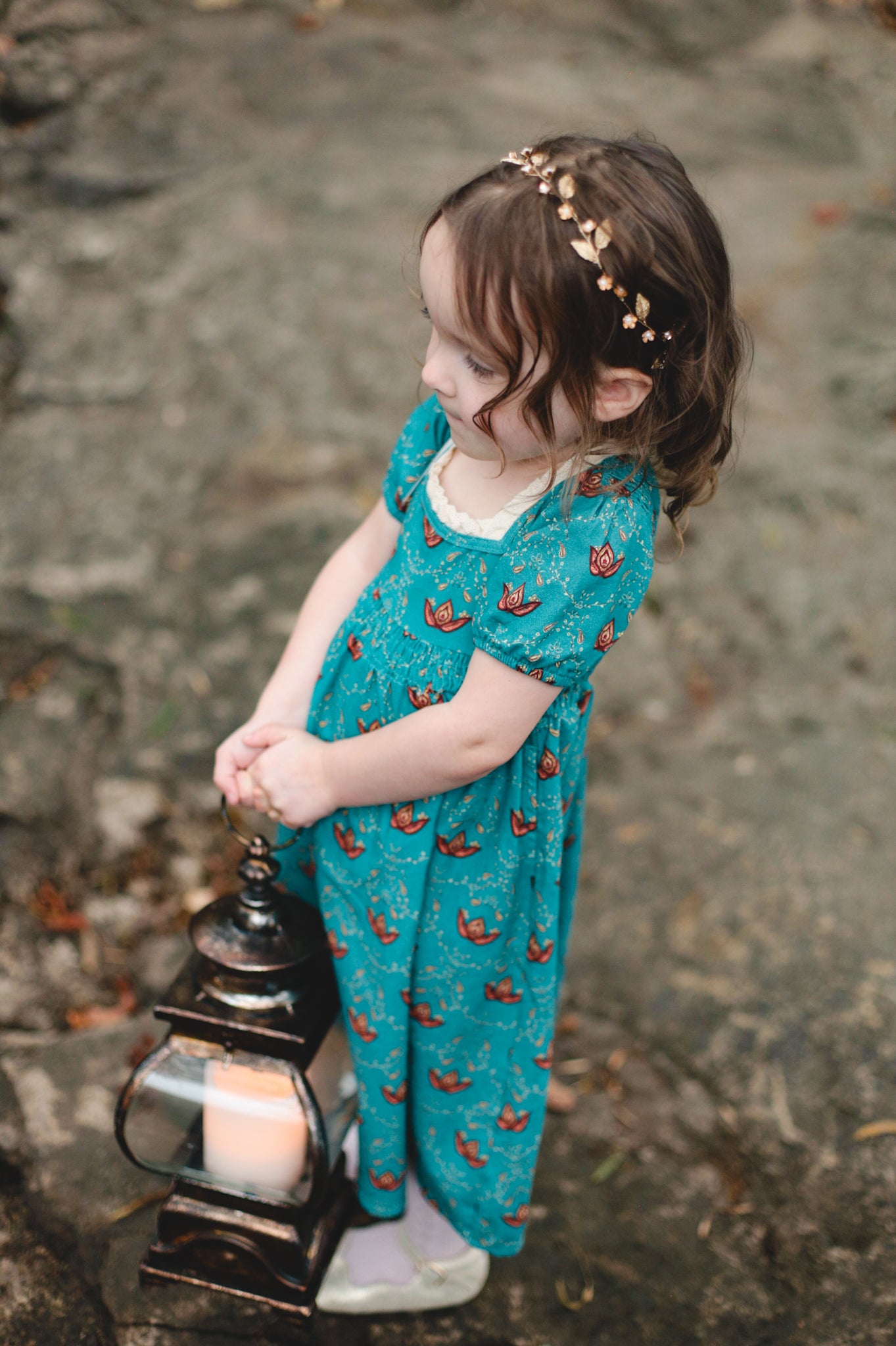 Child wearing modest dress holding lantern on path.