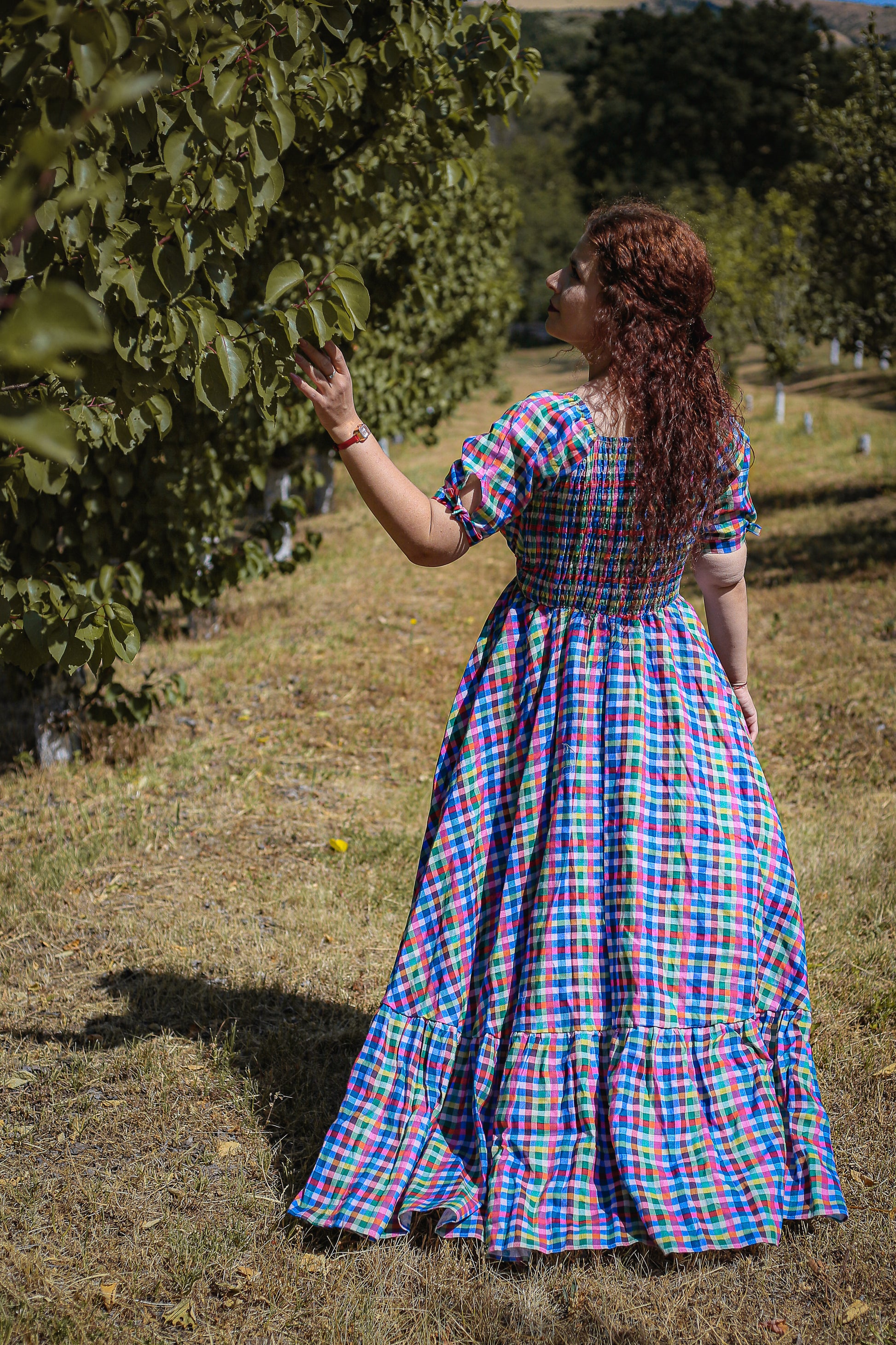 Woman in a colorful modest nursing dress standing in a field with trees in the background
