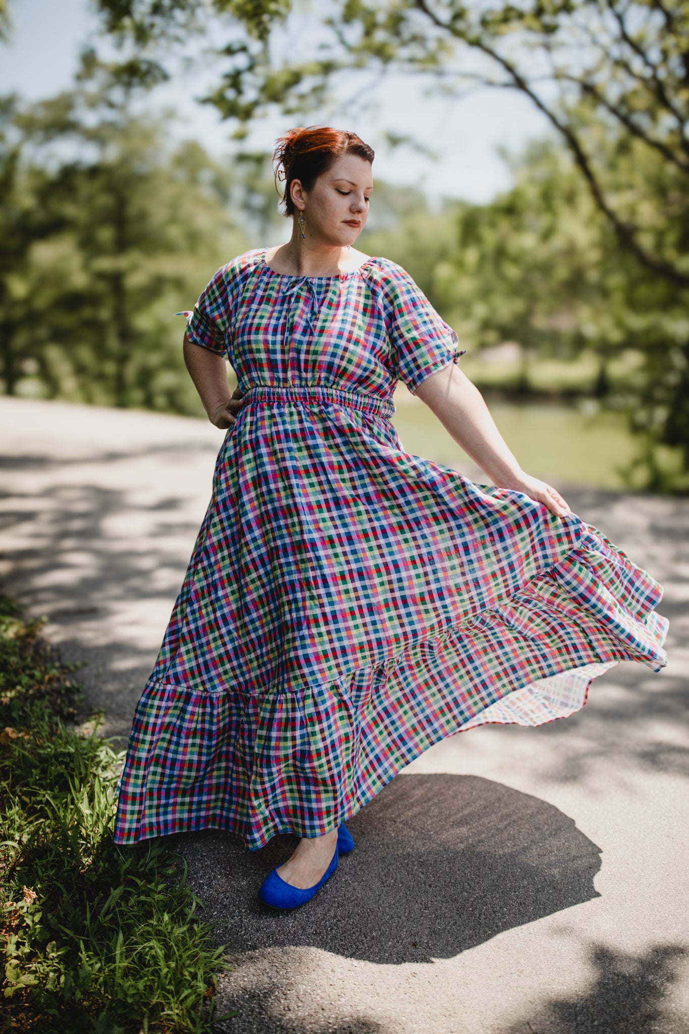 Woman in a plaid modest nursing dress standing outdoors with trees in the background