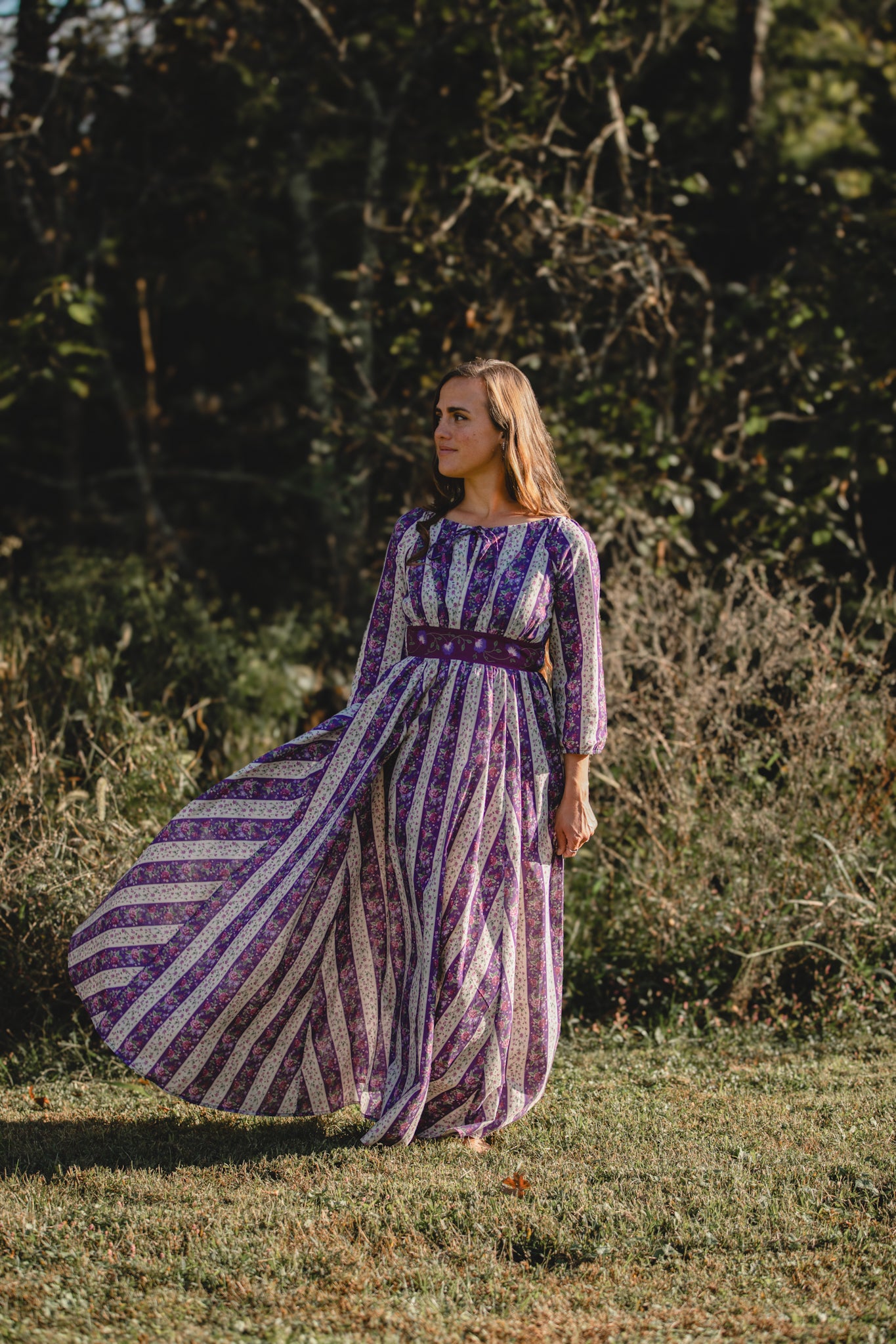 Modest nursing woman in purple striped dress in grassy field
