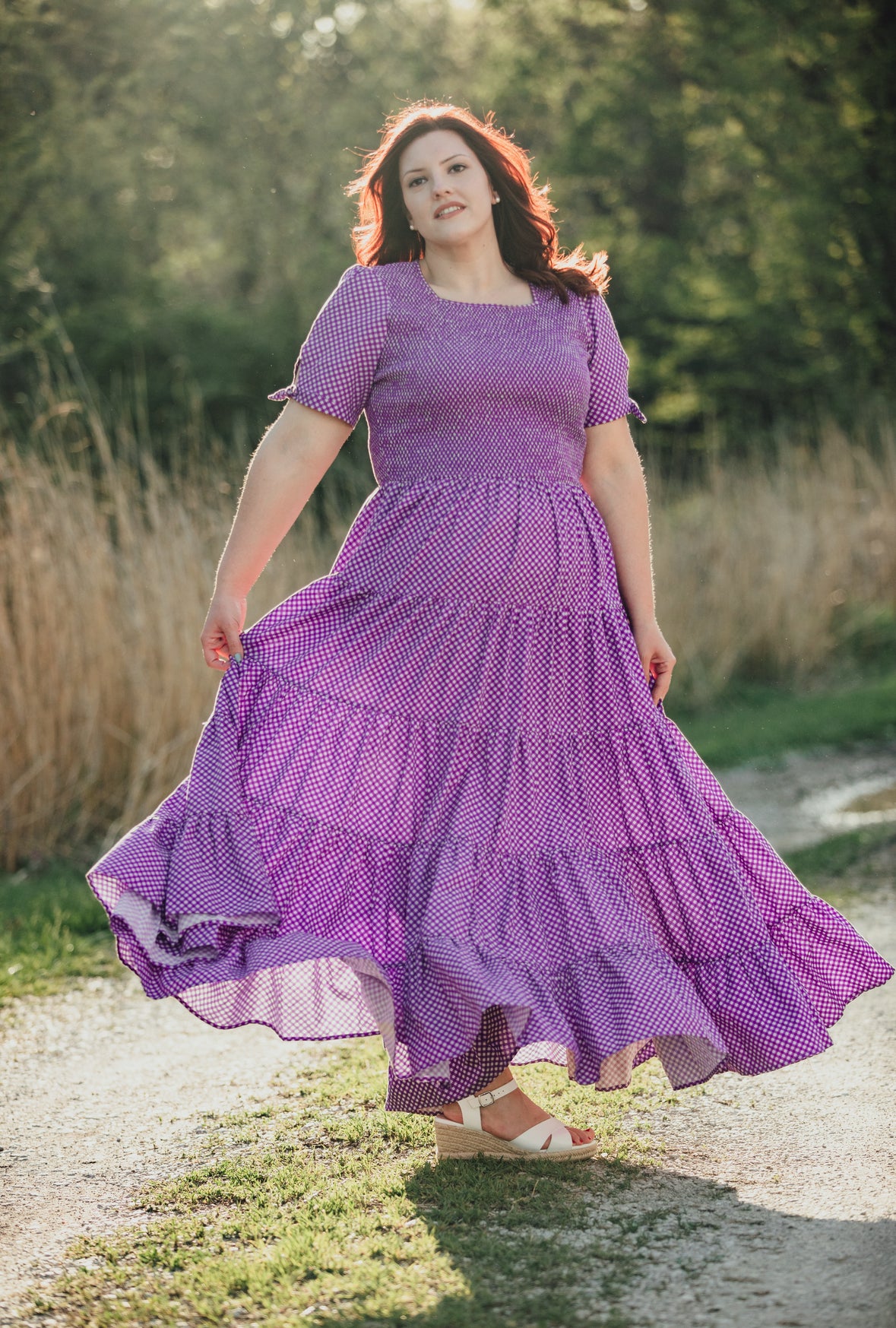 A woman wearing a purple, gingham, five-tiered maxi modest nursing dress