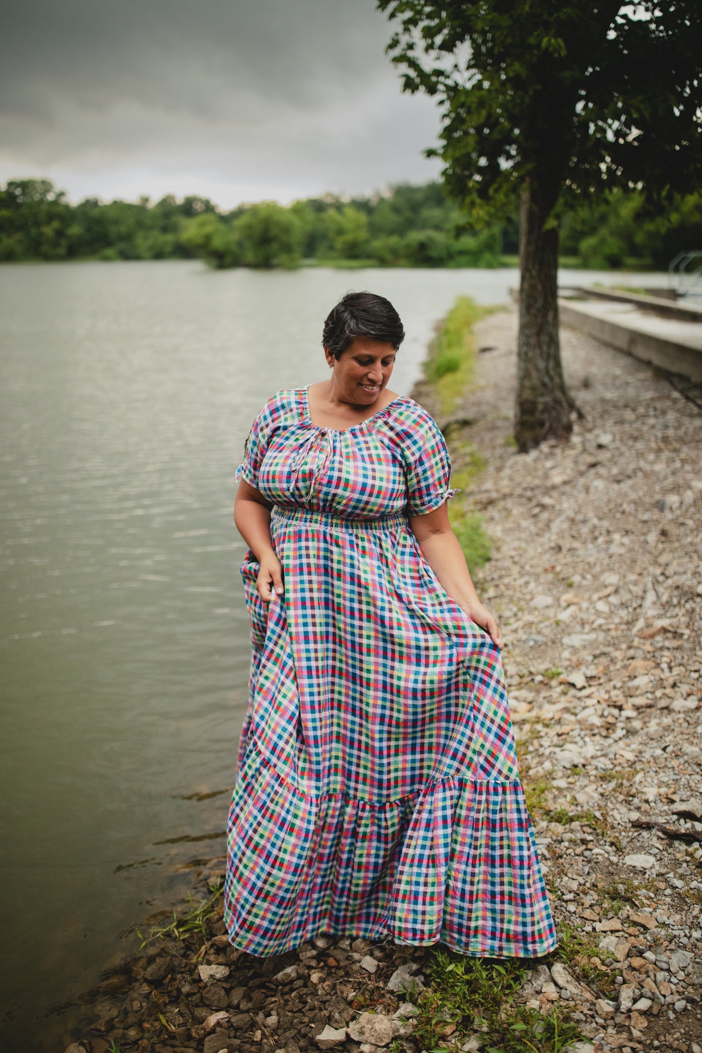 Woman in a plaid modest nursing dress standing by a lake on a cloudy day