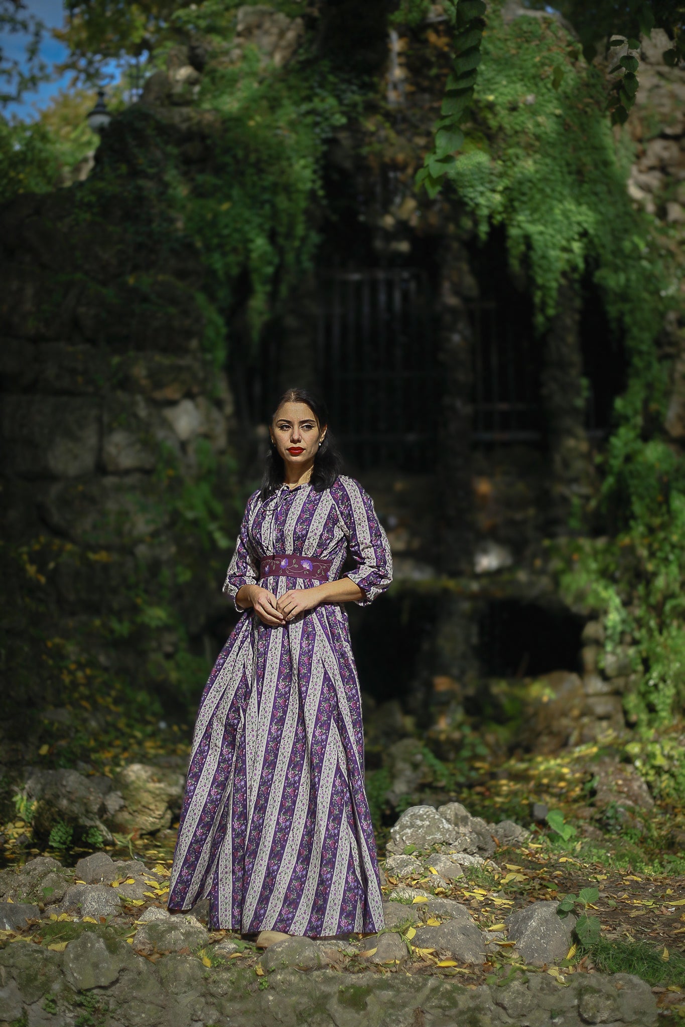 Modest nursing woman in purple striped dress among stone ruins