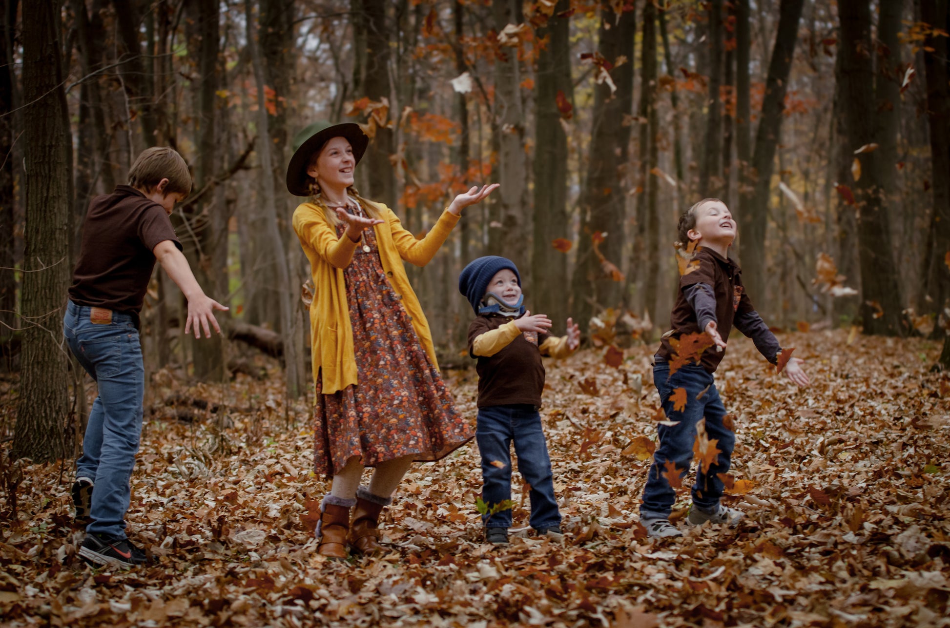 Mother in modest nursing dress with children playing in autumn leaves
