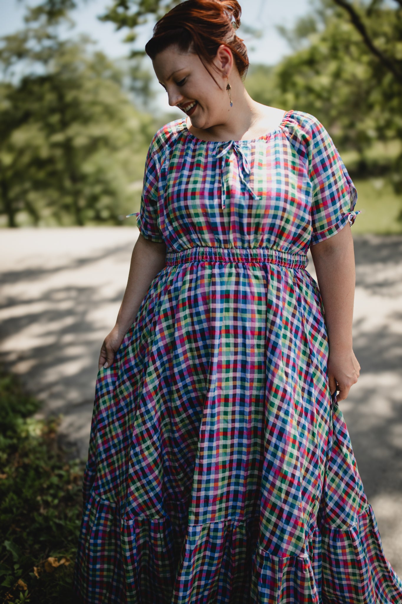 Woman wearing a colorful plaid modest nursing dress standing outdoors with trees in the background