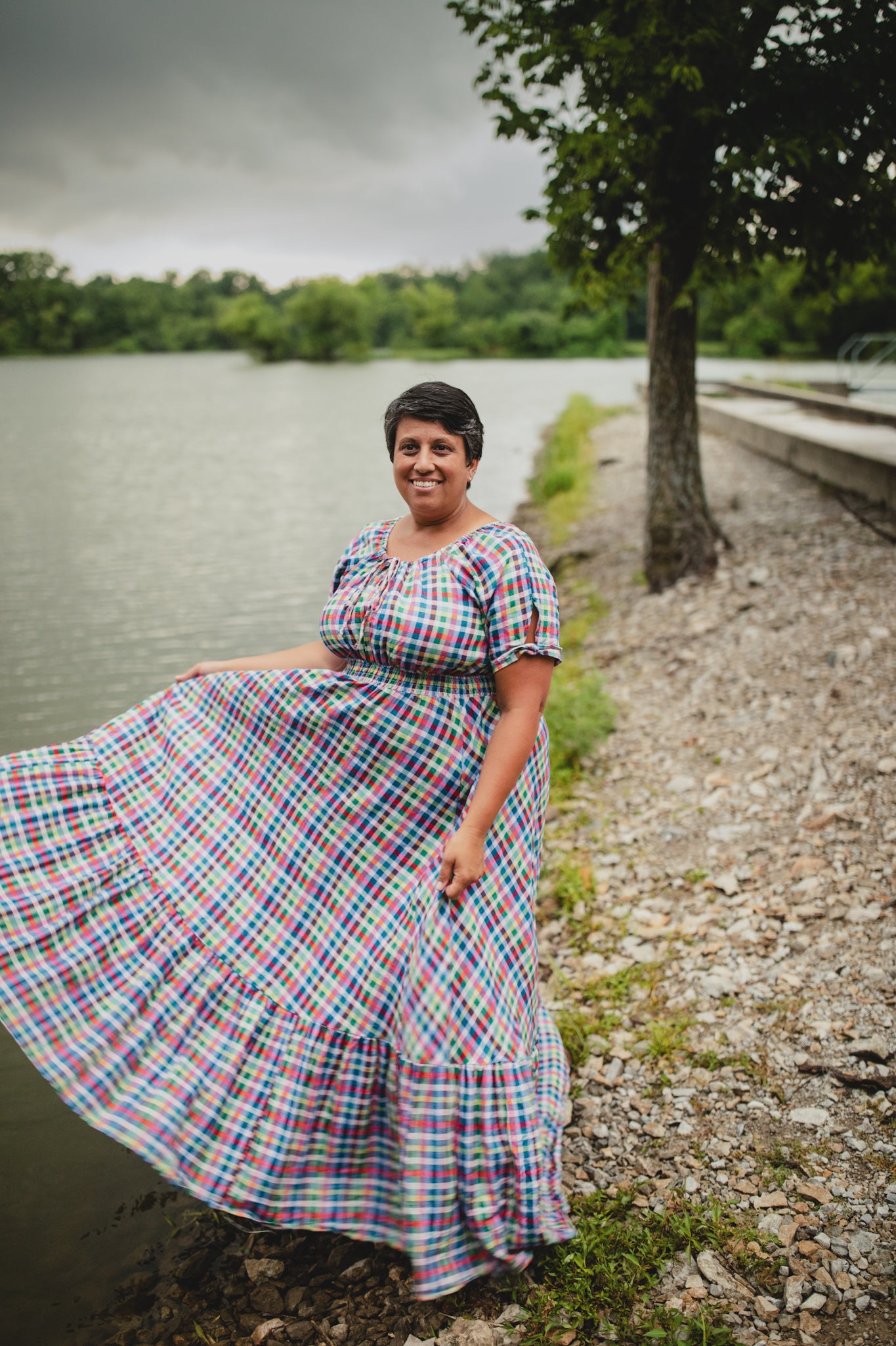 Woman in a colorful modest nursing dress standing by a lake with a tree in the background