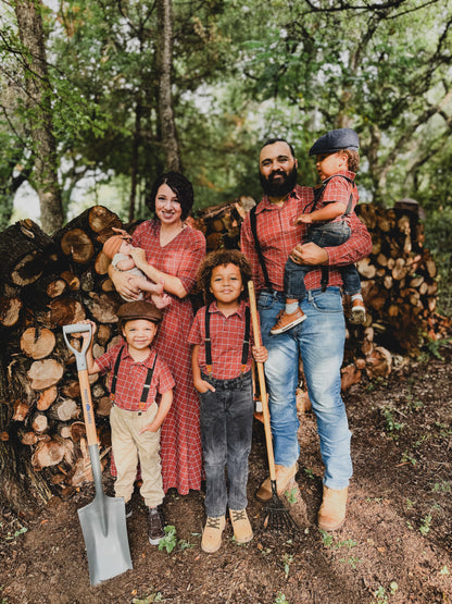 Family of five posing outdoors with a background of stacked wood.