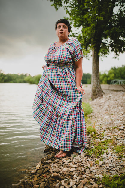 Person wearing a plaid modest nursing dress standing by a body of water with trees in the background
