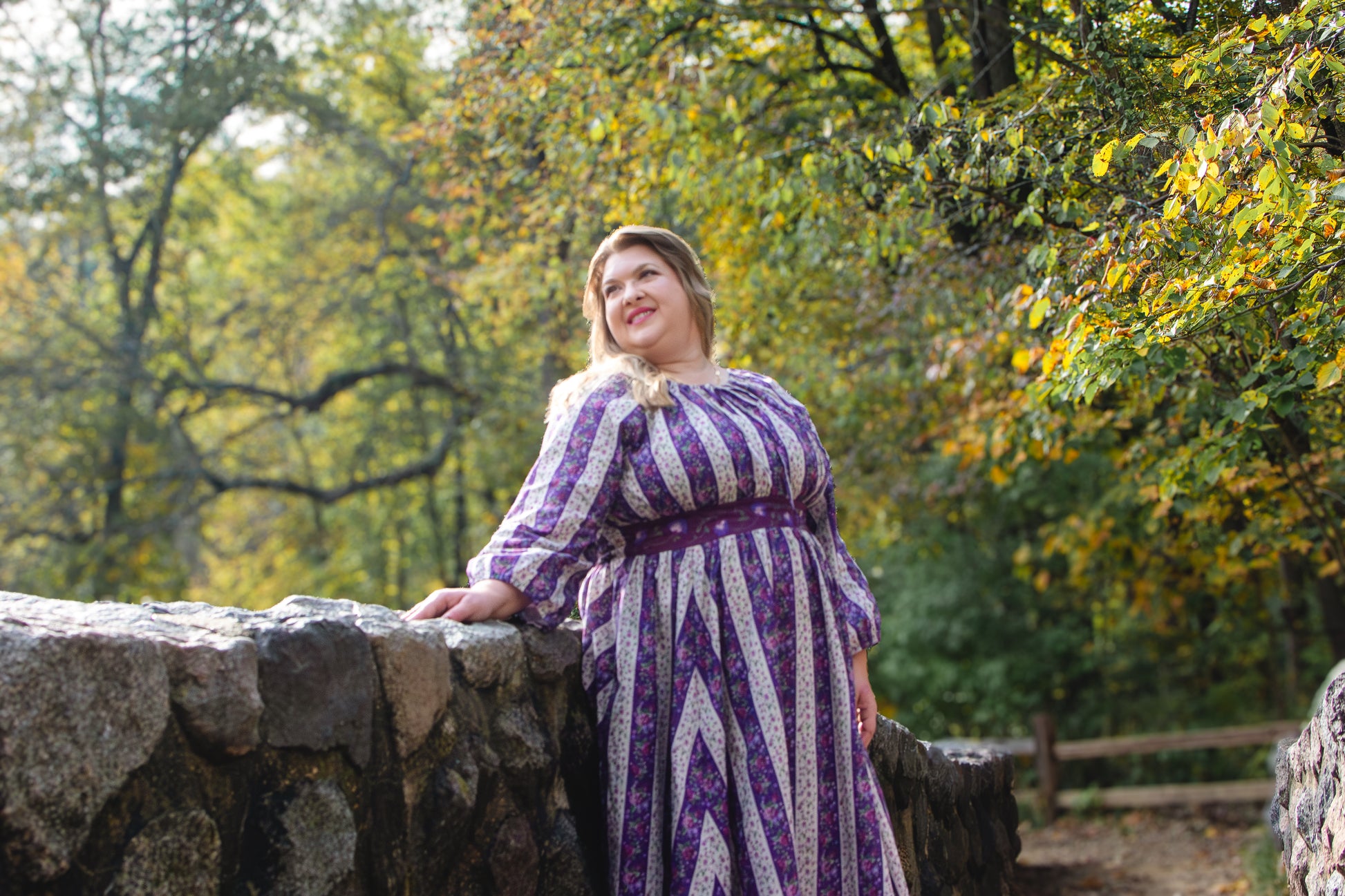 Modest nursing woman leaning on stone wall in purple dress