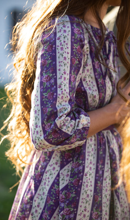 Close-up of a woman wearing a modest nursing purple floral dress with long hair.