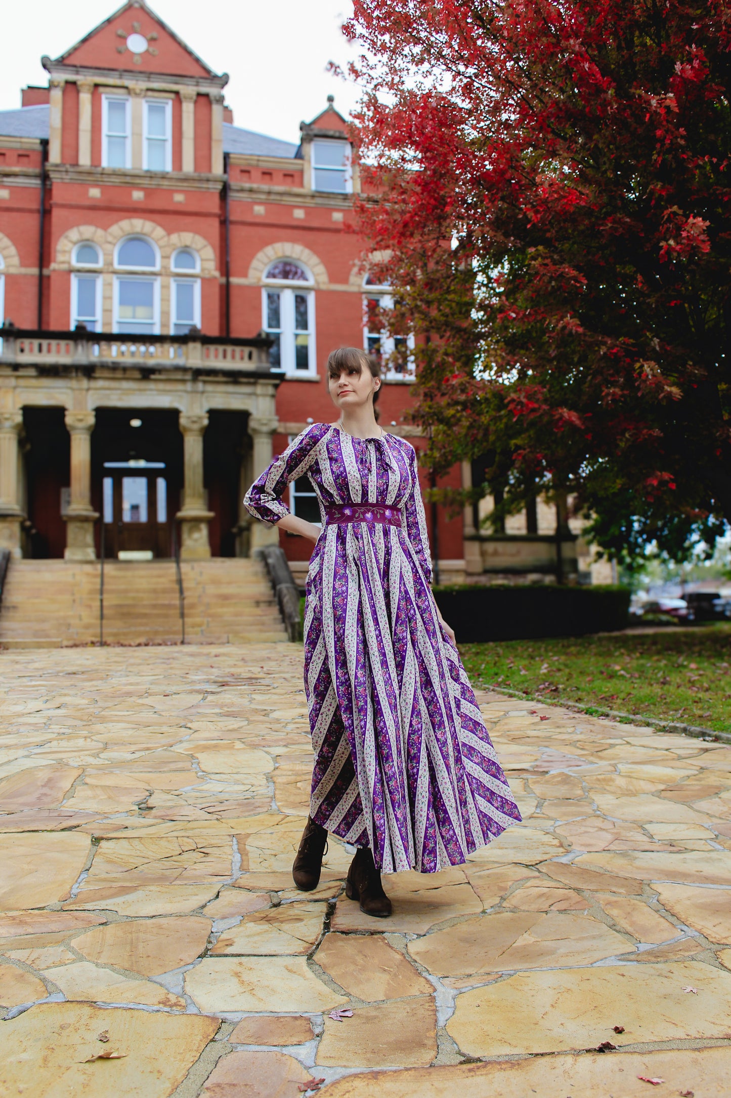 Modest nursing woman in purple dress near red brick building