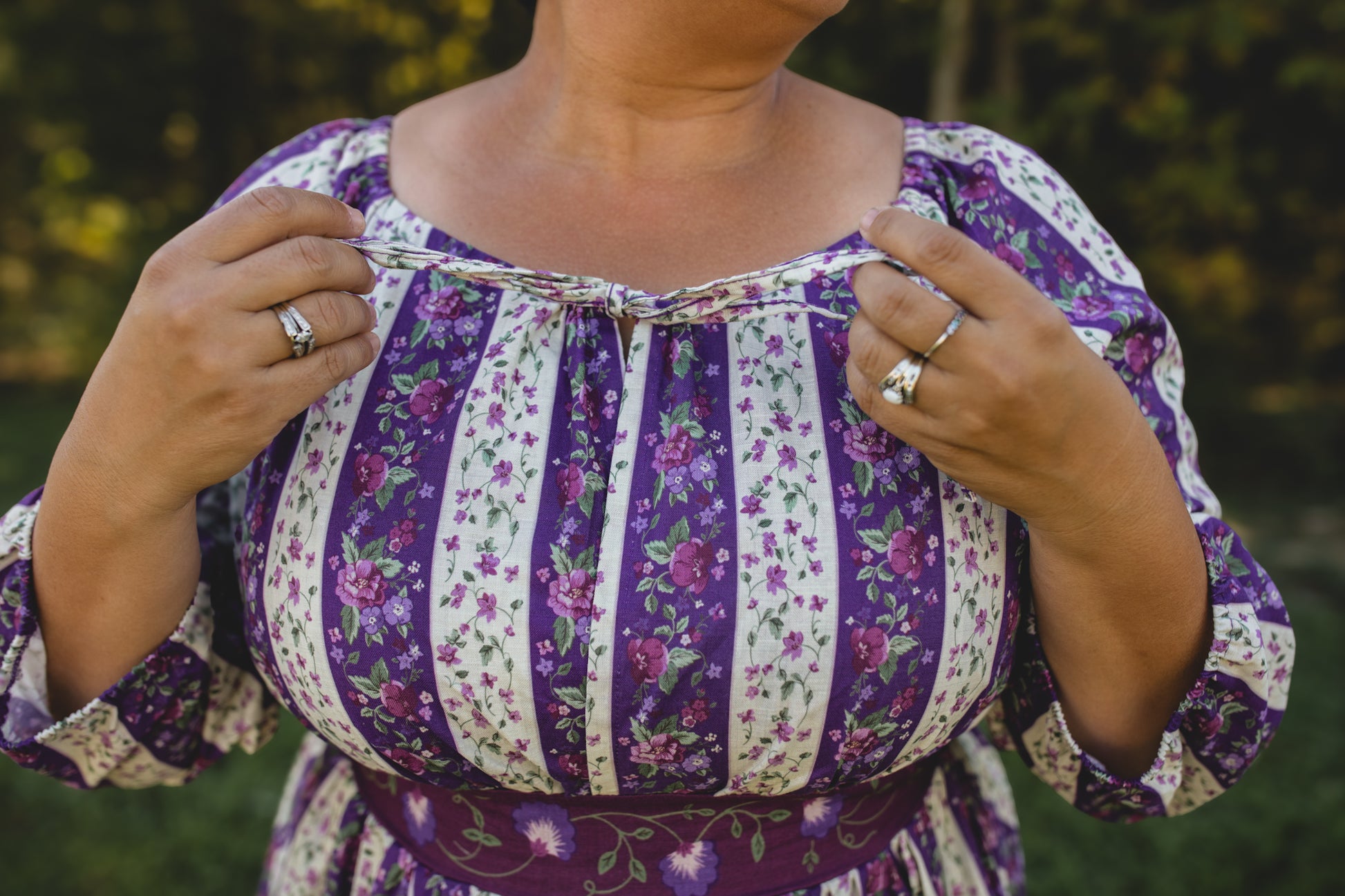 Person wearing a modest nursing purple and white floral dress with a blurred green background