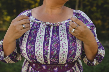 Person wearing a modest nursing purple and white floral dress with a blurred green background