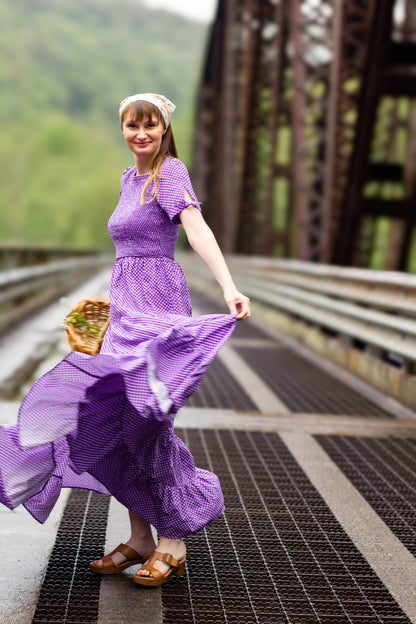 A woman wearing a purple, gingham, five-tiered maxi modest nursing dress