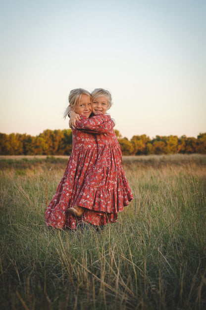 Two children in modest red floral dresses hugging