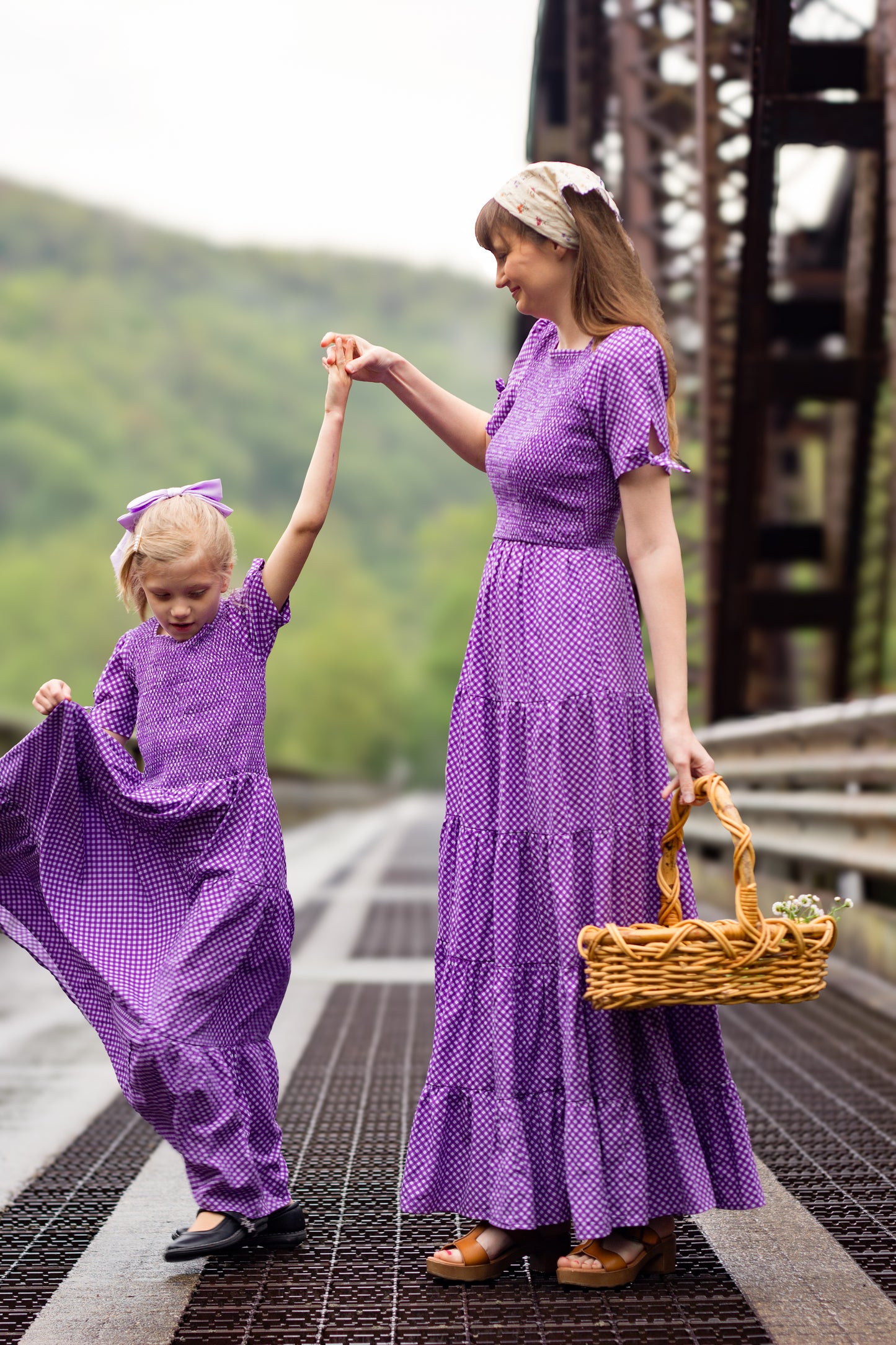 A woman wearing a purple, gingham, five-tiered maxi modest nursing dress with her daughter wearing a matching dress