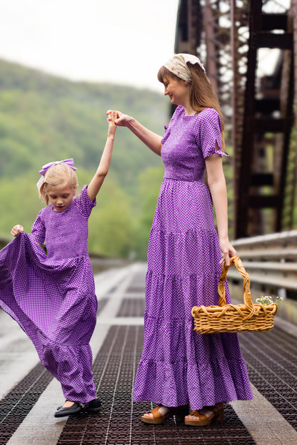 A woman wearing a purple, gingham, five-tiered maxi modest nursing dress with her daughter wearing a matching dress