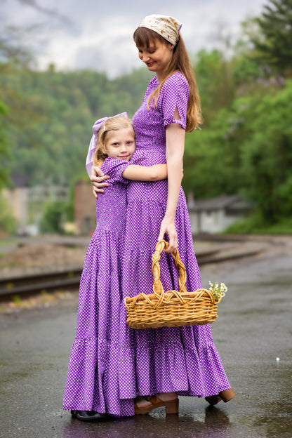 A woman wearing a purple, gingham, five-tiered maxi modest nursing dress with her daughter wearing a matching dress
