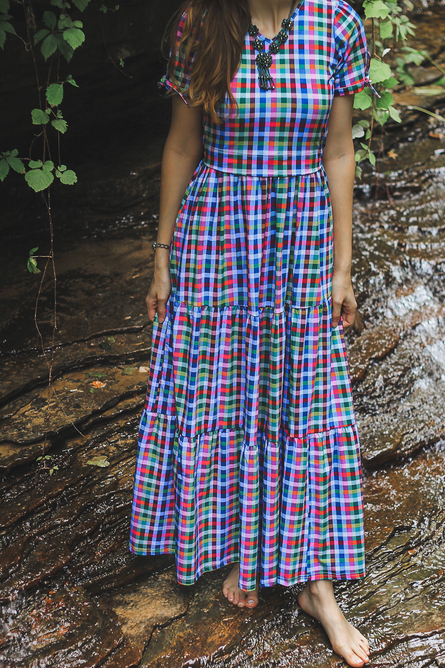 Person wearing a colorful plaid modest nursing dress standing near a stream.