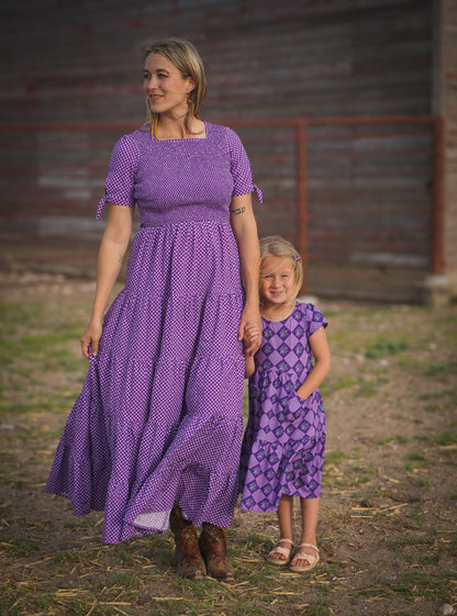 A woman wearing a purple, gingham, five-tiered maxi modest nursing dress with her daughter wearing a matching dress