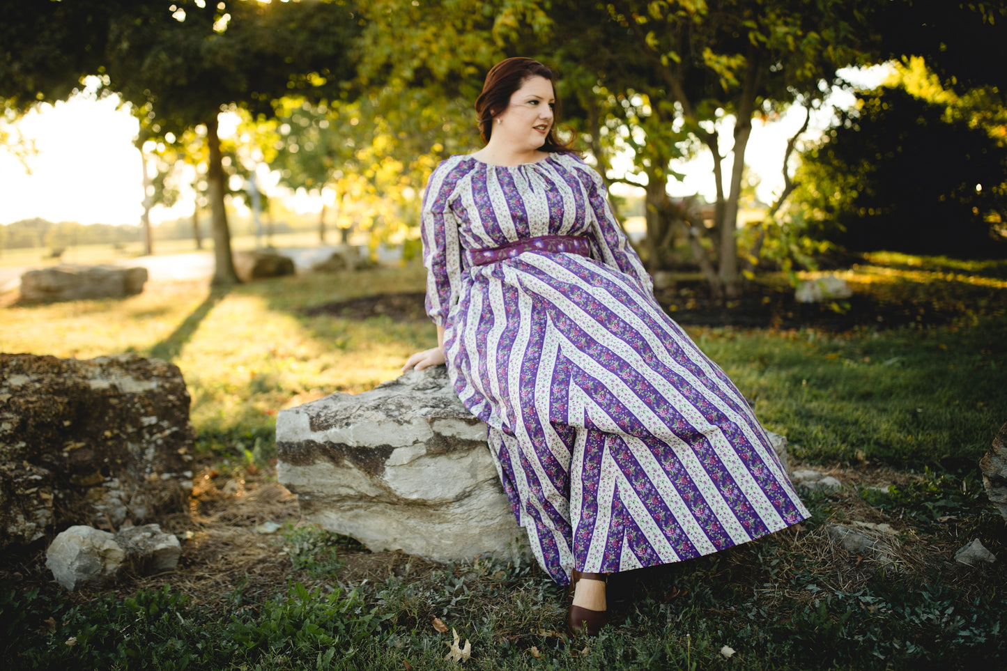 Modest nursing woman in striped dress sitting on rock