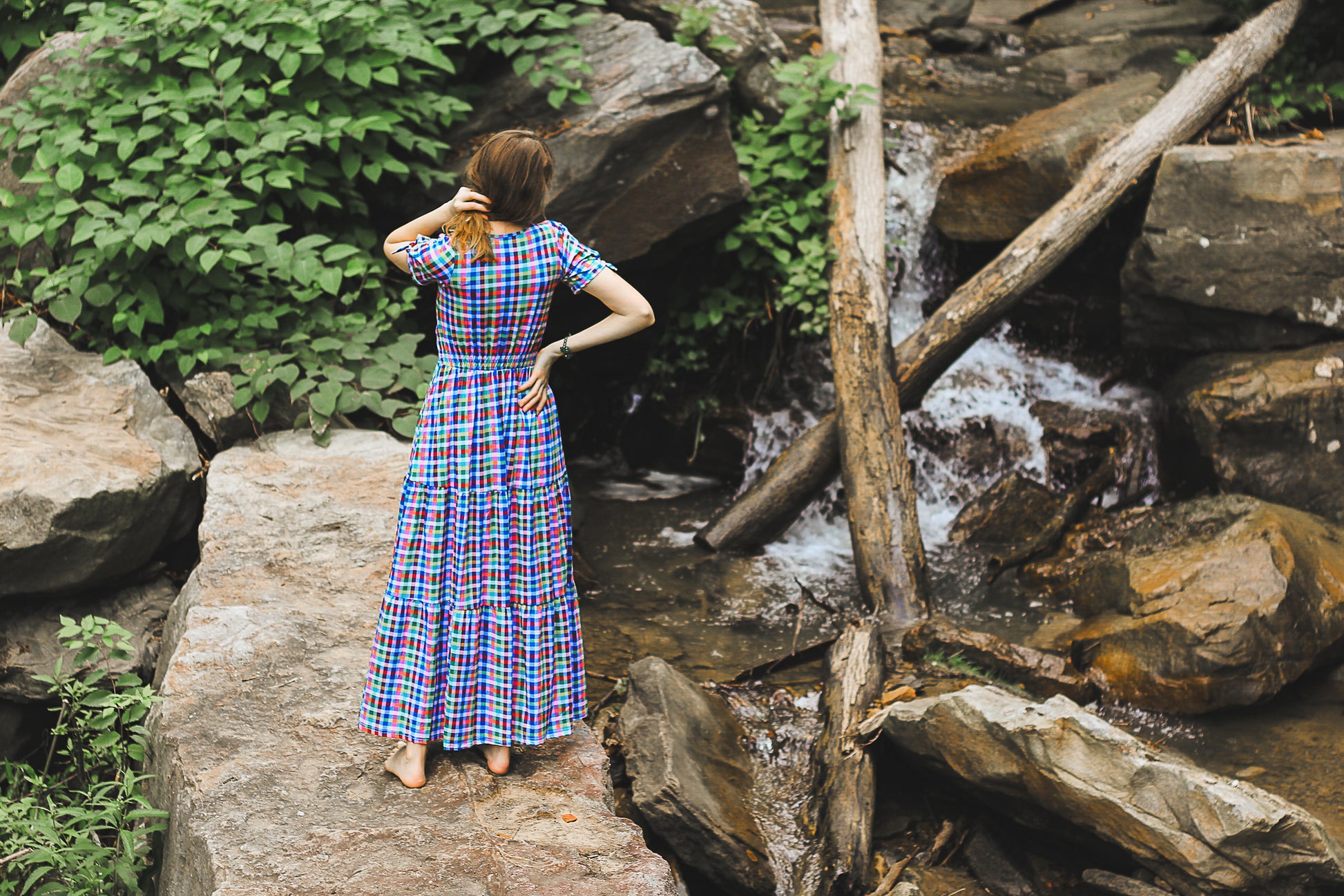 Woman in a plaid modest nursing dress standing on rocks near a waterfall