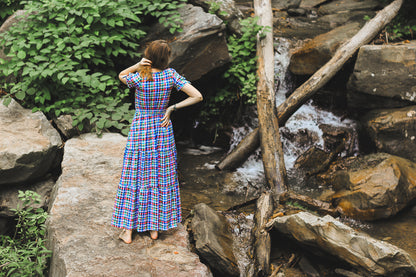 Woman in a plaid modest nursing dress standing on rocks near a waterfall