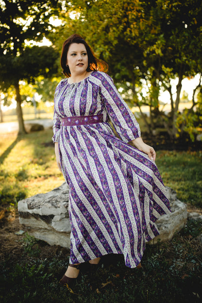 Woman in a modest nursing purple and white striped dress standing outdoors with trees in the background