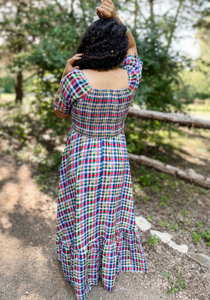 Person wearing a colorful plaid modest nursing dress standing outdoors with trees in the background