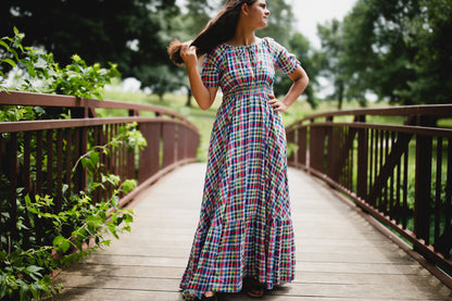 Woman in a plaid modest nursing dress standing on a wooden bridge with greenery around