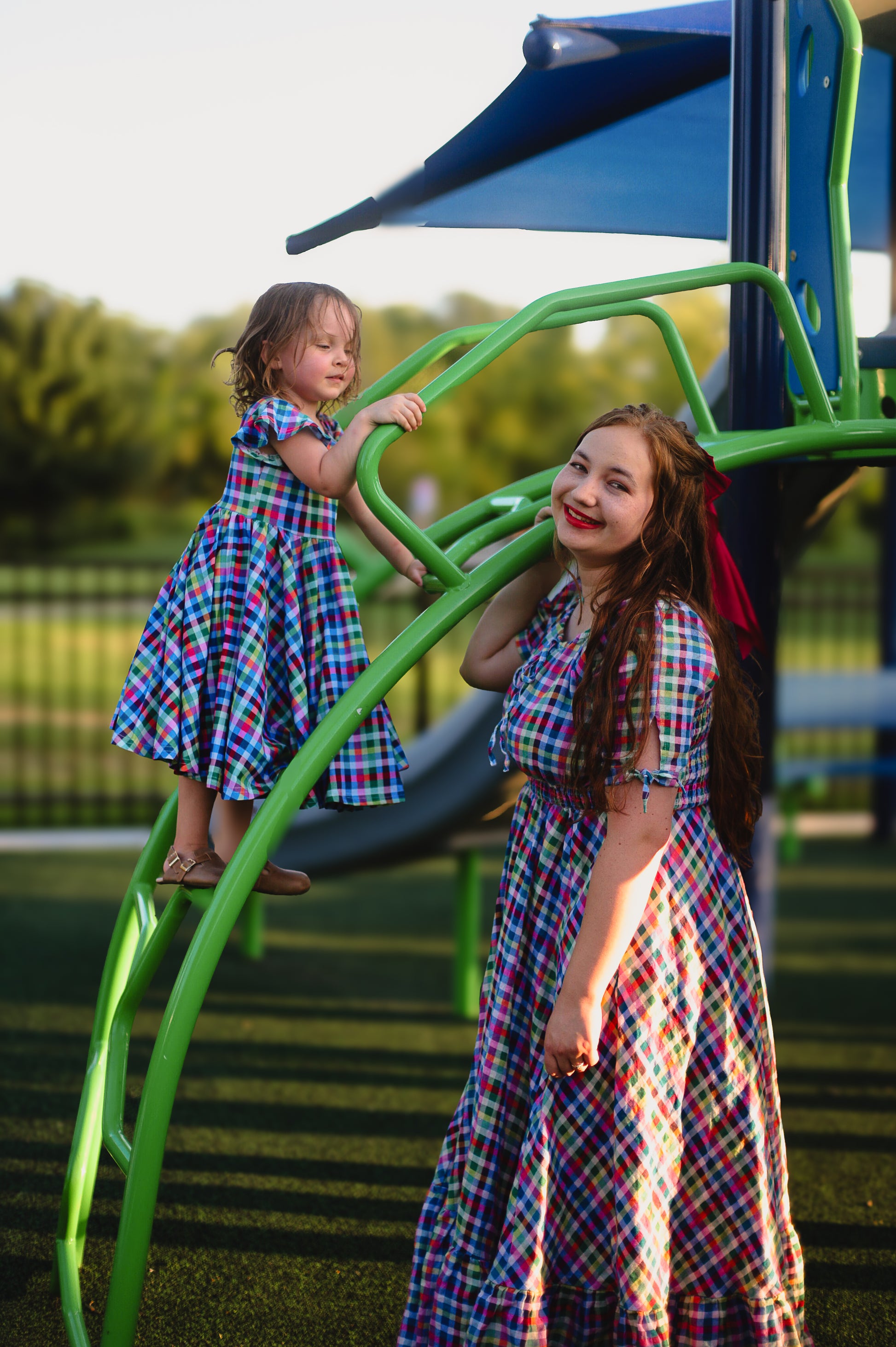 Mother and child in matching plaid modest dresses on a playground slide.