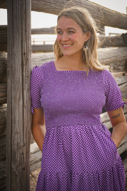 A woman wearing a purple, gingham, five-tiered maxi modest nursing dress