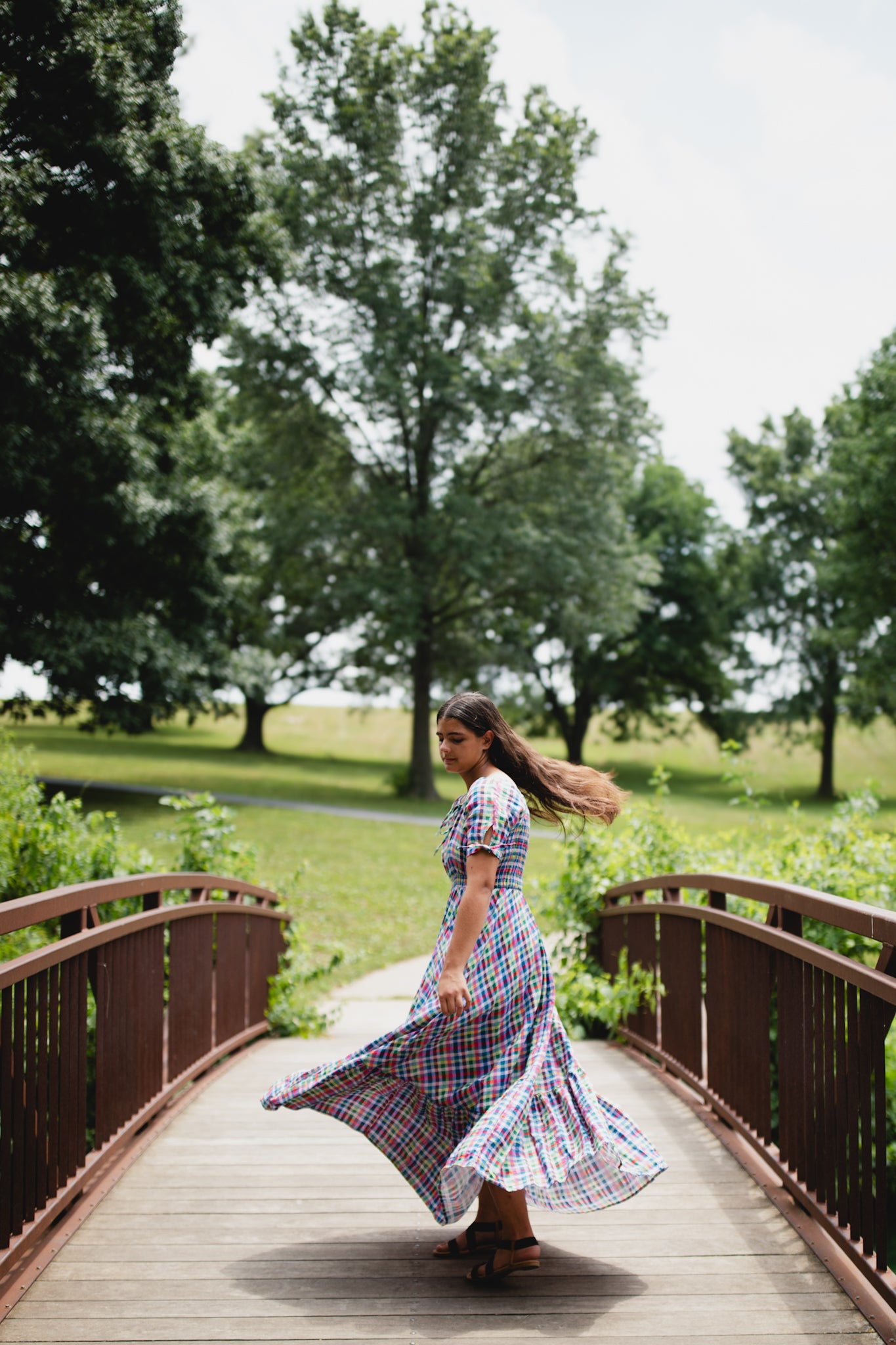 Woman in a plaid modest nursing dress walking on a wooden bridge in a park.